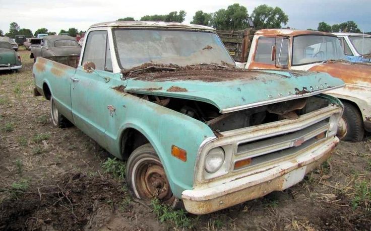 two old trucks are sitting in the dirt and one is rusted out with mud on it's hood