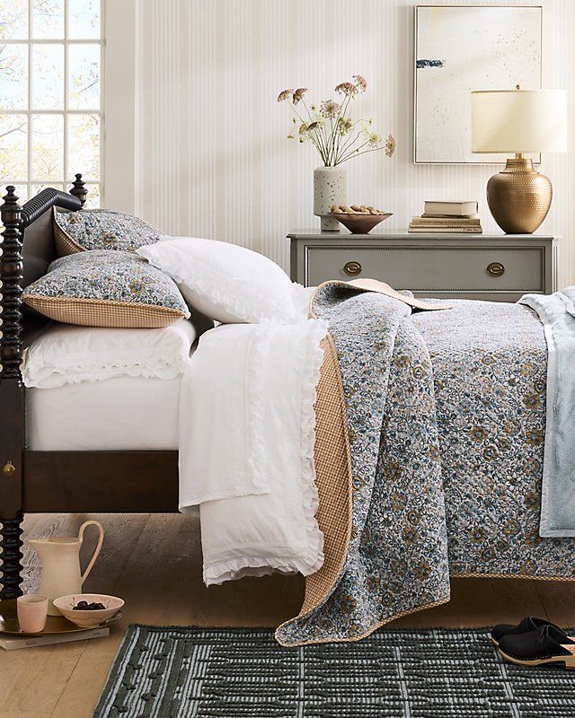 a bed with white sheets and pillows in a bedroom next to a dresser filled with vases