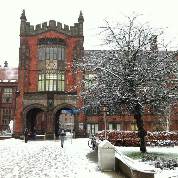 people walking in front of an old building with snow on the ground and trees around it