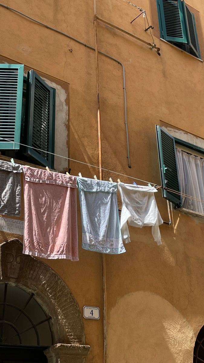 clothes hanging out to dry in front of a building with green shutters and windows