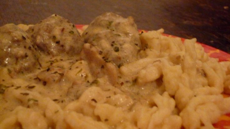 pasta with meatballs and gravy on an orange and pink plate sitting on a table