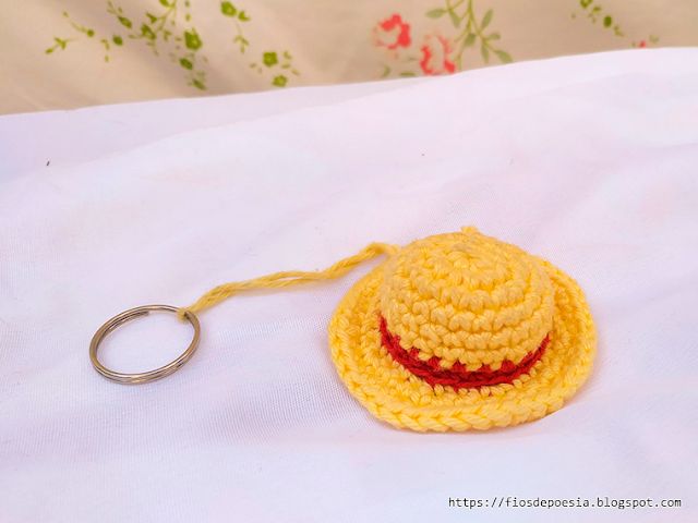 a crocheted yellow hat with a red stripe on the side and a keychain attached to it