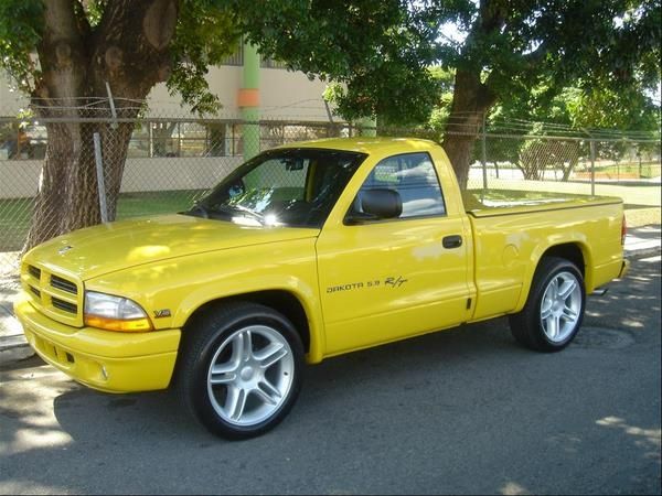 a yellow pick up truck parked on the side of the road in front of a tree