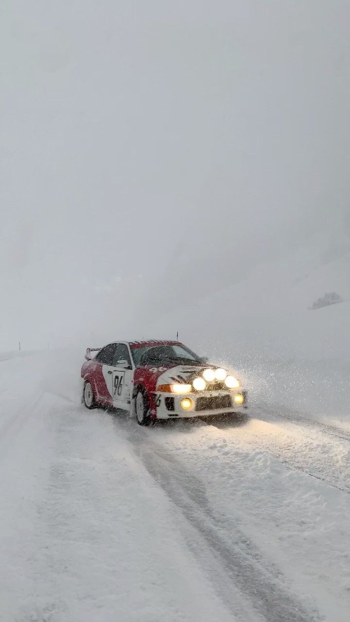 a car driving down a snow covered road in the middle of the day with headlights on