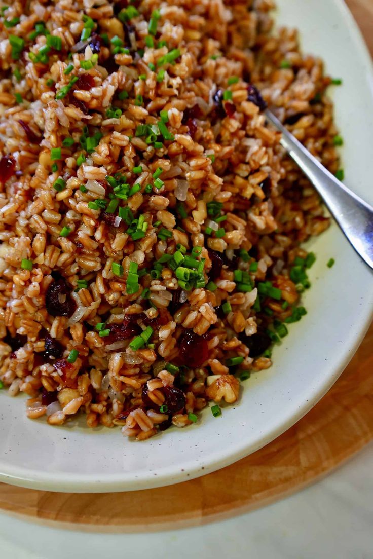 a white plate topped with brown rice and veggies next to a silver spoon