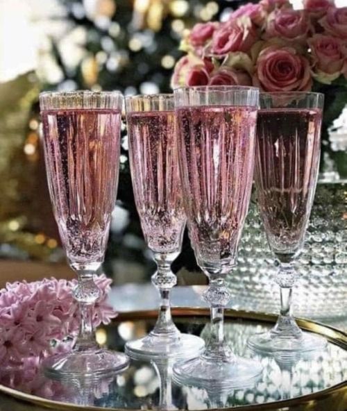 three wine glasses sitting on top of a table next to pink flowers and vases