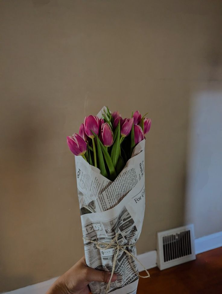 a person holding a bouquet of pink tulips wrapped in newspaper