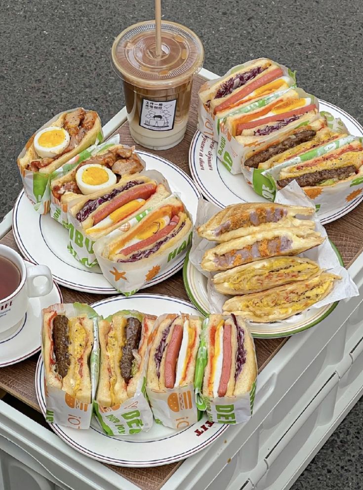 several plates with sandwiches and drinks on them sitting on a table next to a trash can