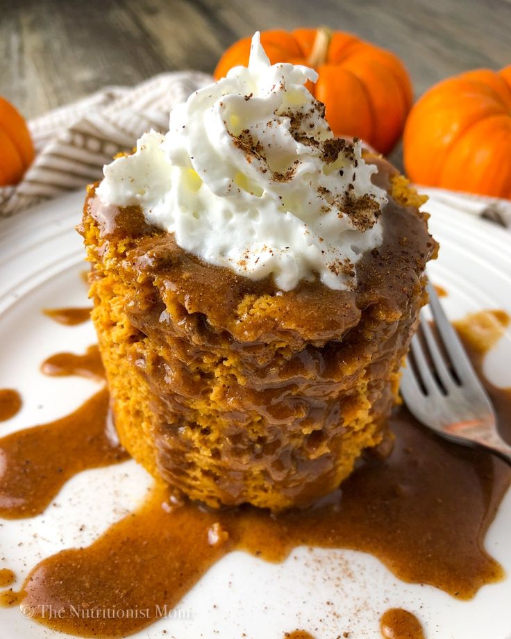 a close up of a piece of cake on a plate with whipped cream and pumpkins in the background