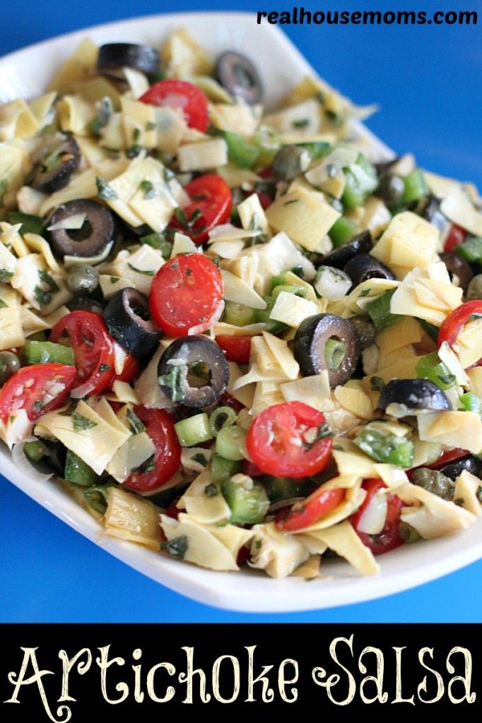 an artichoke salad with tomatoes, olives and peppers in a white serving dish