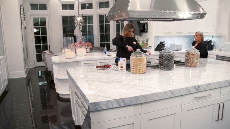 two women in a kitchen preparing food on a counter top with an oven hood over the stove