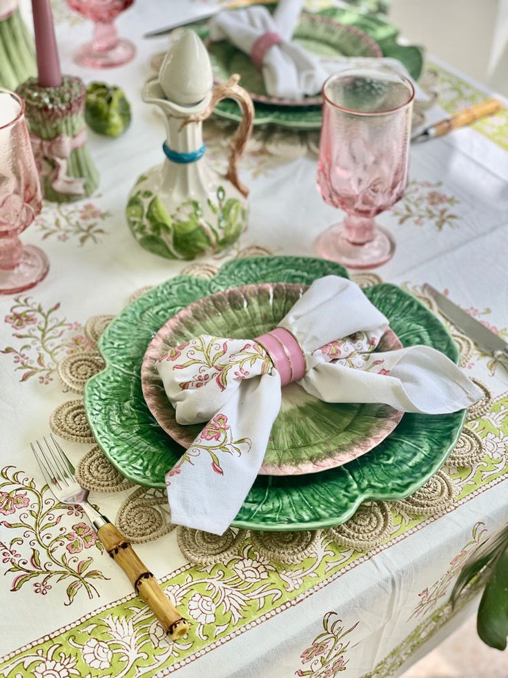 the table is set with pink and green plates, napkins, and silverware