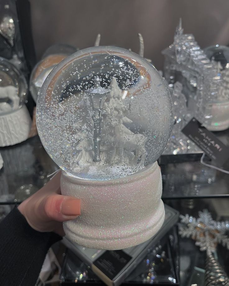 a snow globe is being held up in front of other christmas decorations and ornaments on display