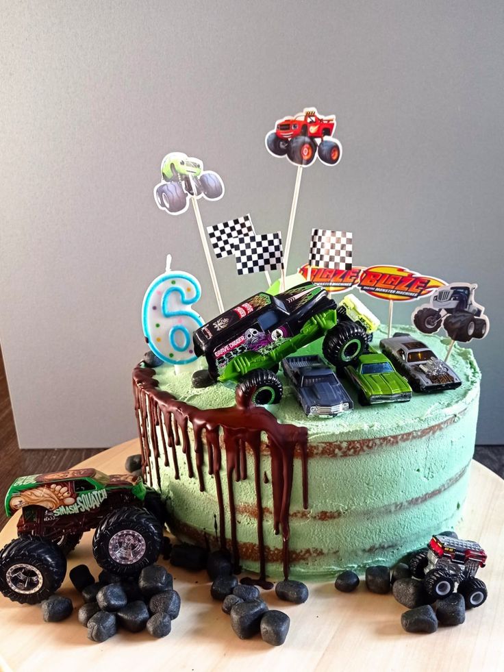 a birthday cake with monster trucks and cars on it's icing drips