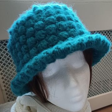 a white mannequin head wearing a teal colored knitted cloche hat