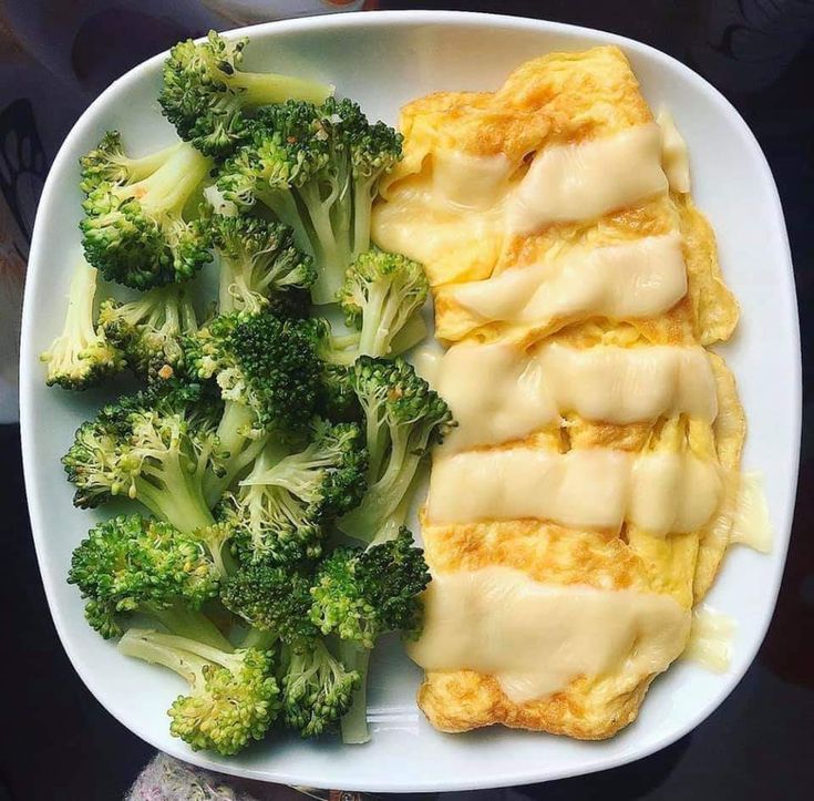 a white plate topped with broccoli covered in cheese