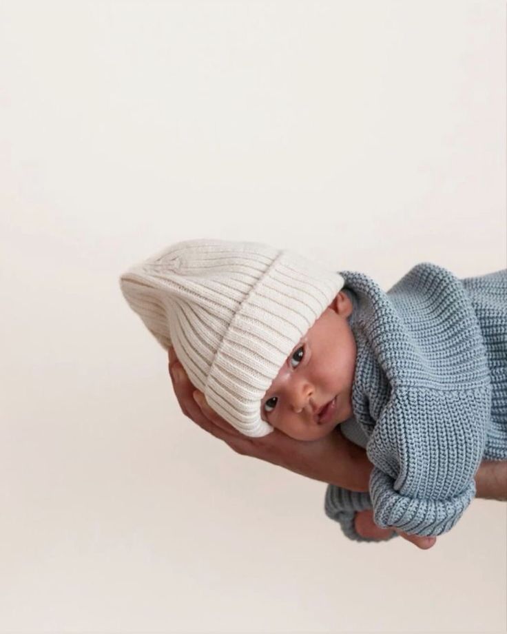 a baby in a knitted hat being held by someone's hand with a white background