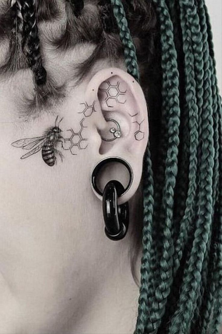 a woman's ear with some piercings on top of her ears and two bees behind the ear