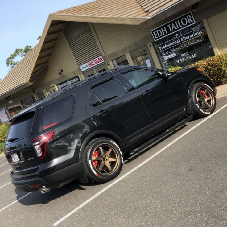 a black suv is parked in front of a building with red rims and gold wheels