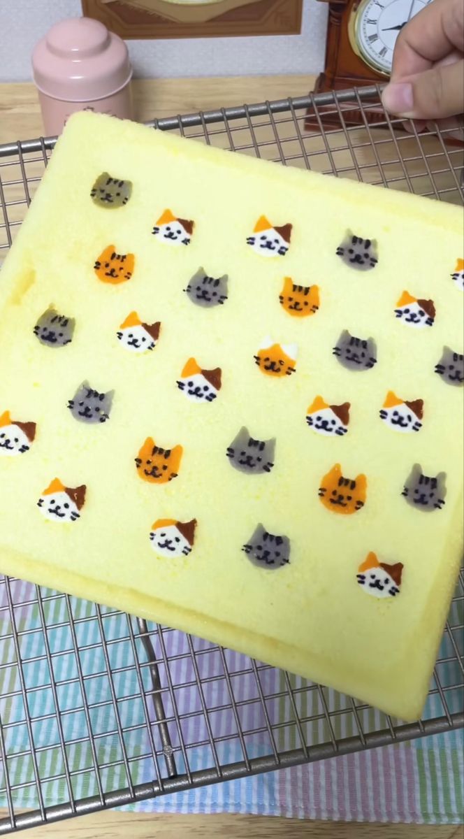 a cake with cats on it sitting on a cooling rack next to an alarm clock