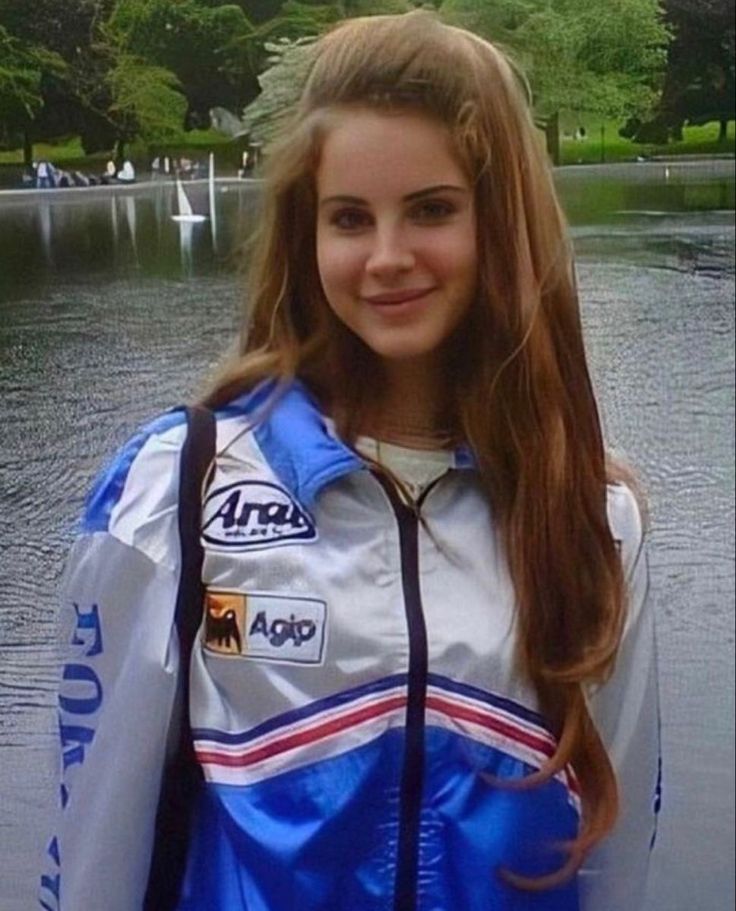 a young woman standing in front of a body of water wearing a blue and white jacket