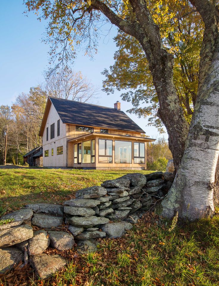 a small house sitting on top of a lush green field next to a tree and stone wall