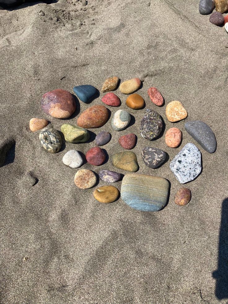 rocks arranged in the shape of a heart on a sandy beach next to a person's shadow