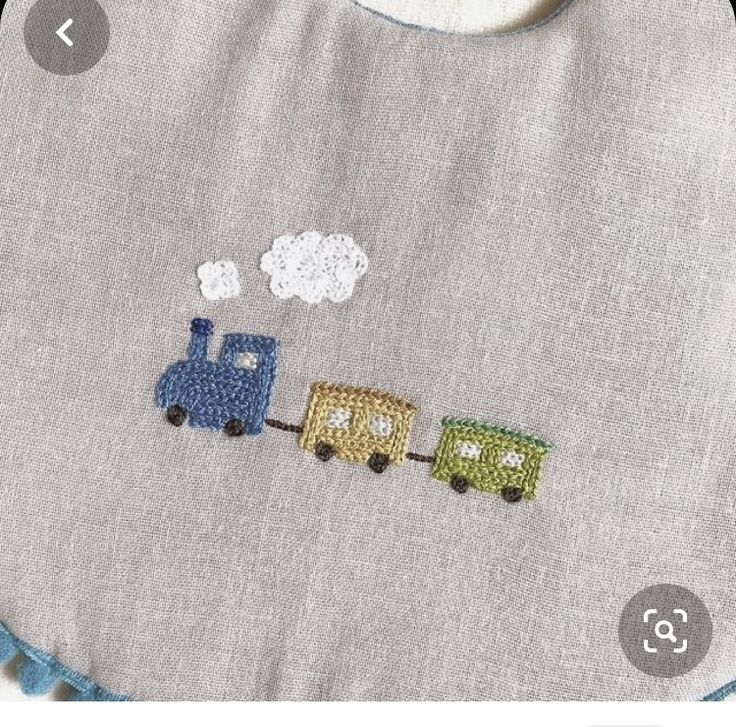 an embroidered bib with a train on it and clouds in the sky behind it