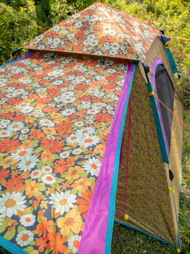 a colorful tent is set up in the grass with trees behind it and flowers all over