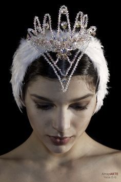 a woman wearing a tiara with white feathers and jewels on her head is looking down