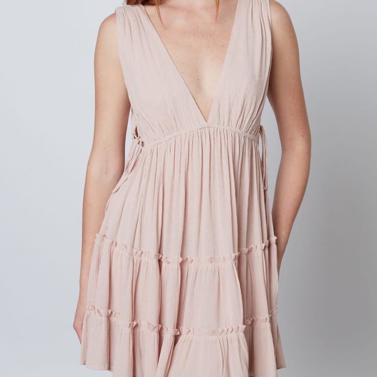 This Deep V Swing Dress Showcases An Alluring Silhouette With Beautiful Ruffle And Lace Up Side Cut Out Details. Perfect For A Beach Or Boho Look, This Dress Will Make You Stand Out In Any Occasion. Self 100% Rayon Breezy Mini Dress For Beach Cover-up, Chic V-neck Beach Dress For Summer Outings, Breezy V-neck Mini Dress For Day Out, V-neck Sundress For Summer Outings, Chic V-neck Sundress For Summer Outings, Summer Tiered Beach Dress, Beige Mini Boho Dress For Vacation, Beige Boho Mini Dress For Vacation, Flowy Mini Dress For Beachwear