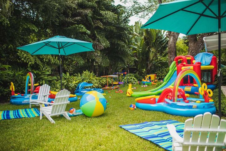 an inflatable pool with chairs, umbrellas and beach balls on the lawn