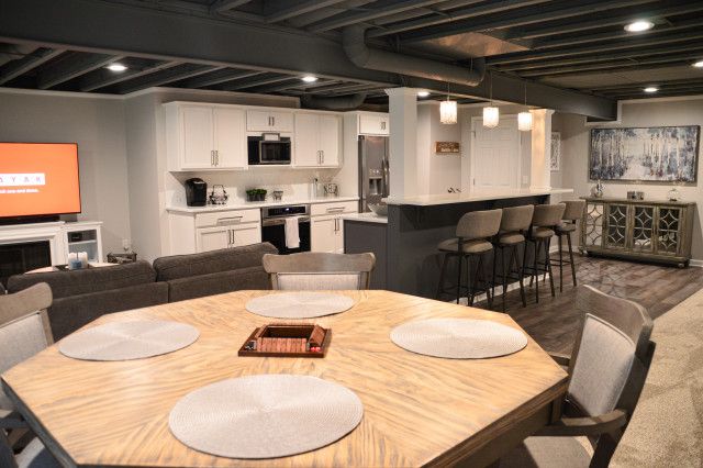 an open concept kitchen and living room with white cabinets, wood dining table and bar stools