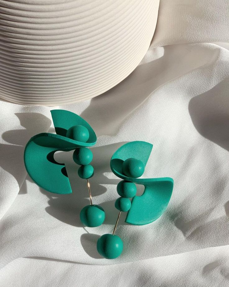 two green earrings sitting on top of a white cloth next to a cup and saucer