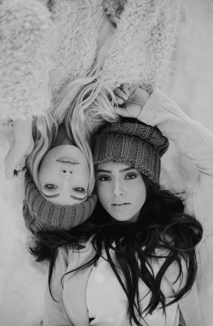 two young women laying on top of each other wearing hats and scarves with their hands behind them