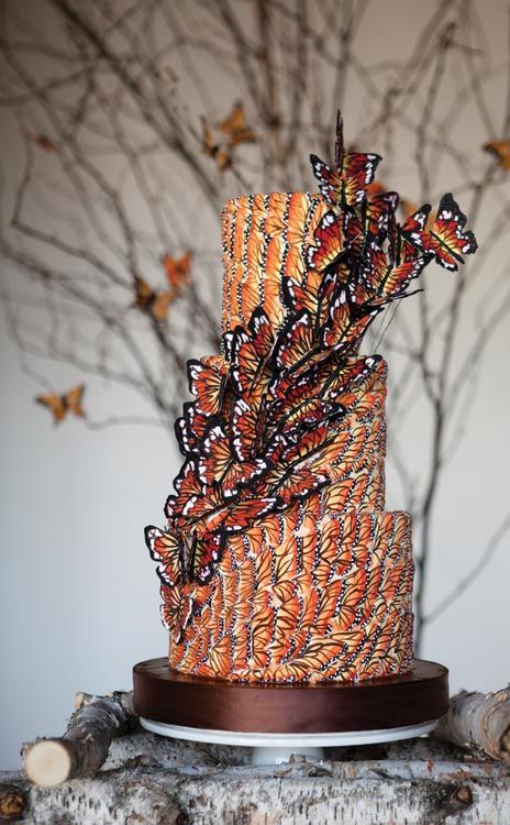 a multi layer cake decorated with butterflies on top of a wooden table next to branches