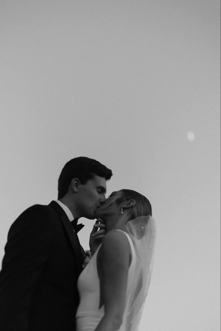 a bride and groom kissing in front of the sky