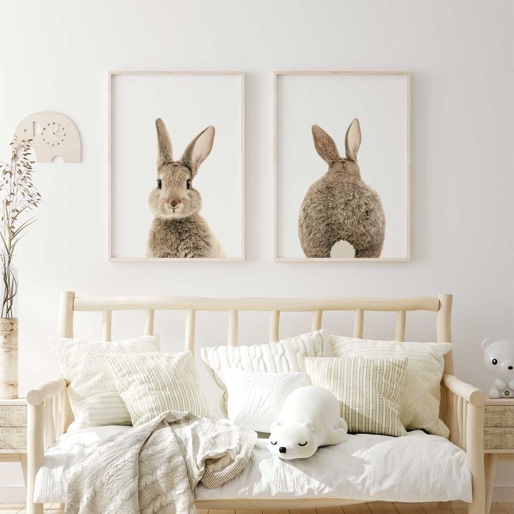 two pictures of rabbits hanging on the wall above a bed with pillows and blankets,