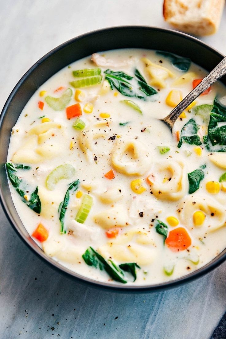 a bowl filled with pasta and vegetables next to a piece of bread on a table