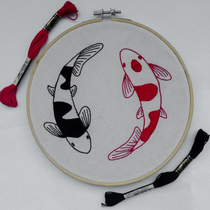 two black and white koi fish in a circle with red thread on the hoop