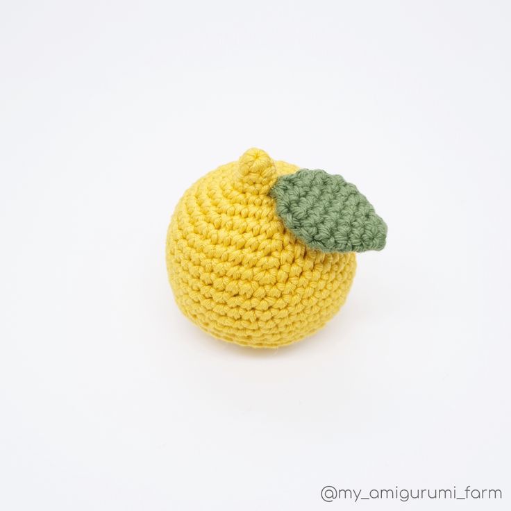 a crocheted lemon with a green leaf on it's tip sits against a white background