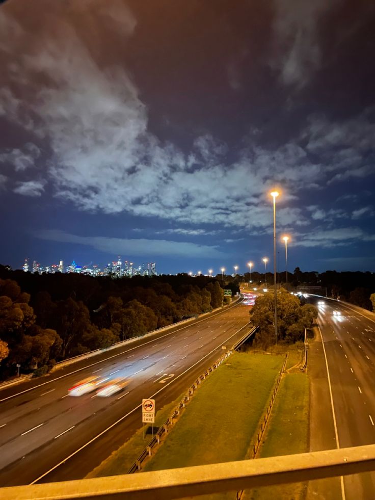 an empty highway at night with cars driving on the road and street lights in the distance