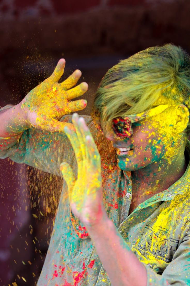 a man covered in yellow and green powder throwing his hands up to the side with colored paint all over his face