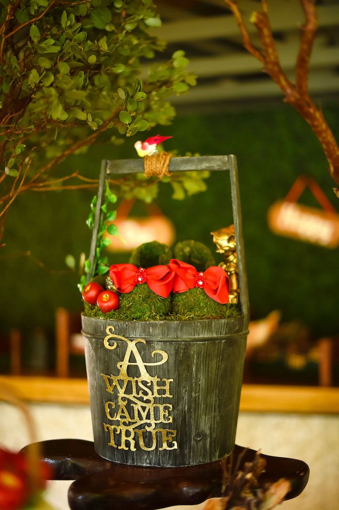 a wooden bucket filled with moss and red flowers on top of a table next to a tree