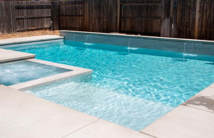 an empty swimming pool with steps leading to the water and a wooden fence in the background