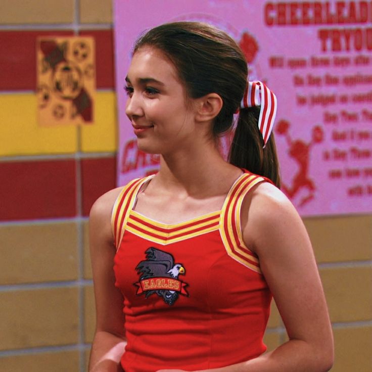 a girl in a cheerleader uniform holding a frisbee and smiling at someone