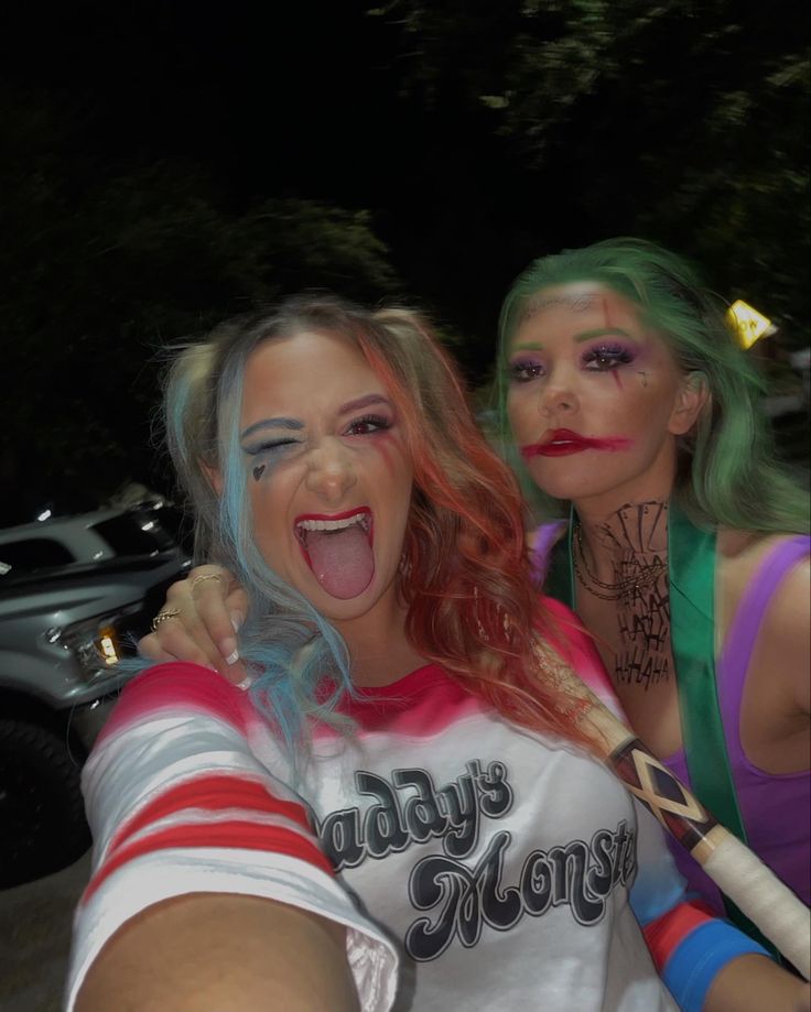 two women with makeup and wigs taking a selfie in front of a car