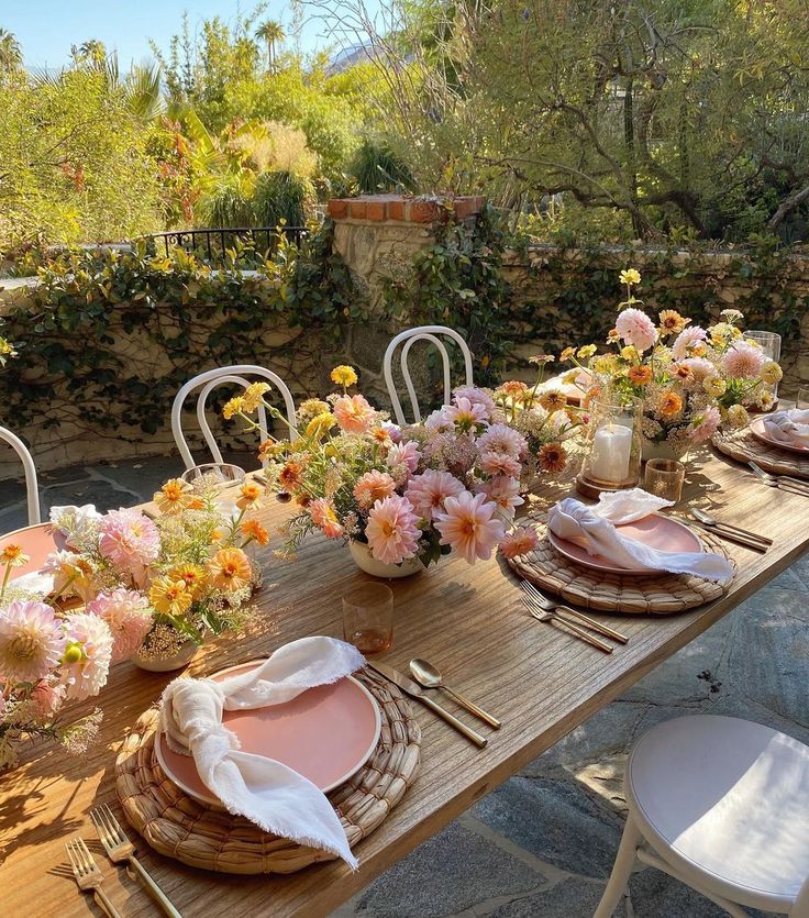 an outdoor table set with plates and flowers