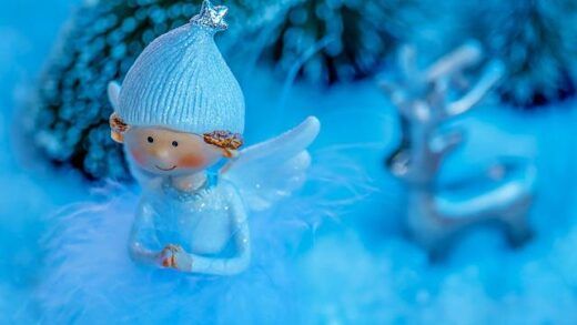 an angel figurine sitting in the snow next to some christmas trees and ornaments