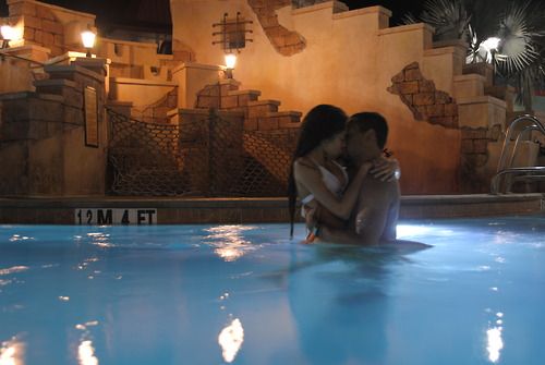 two people sitting in the middle of a swimming pool at night with their arms around each other